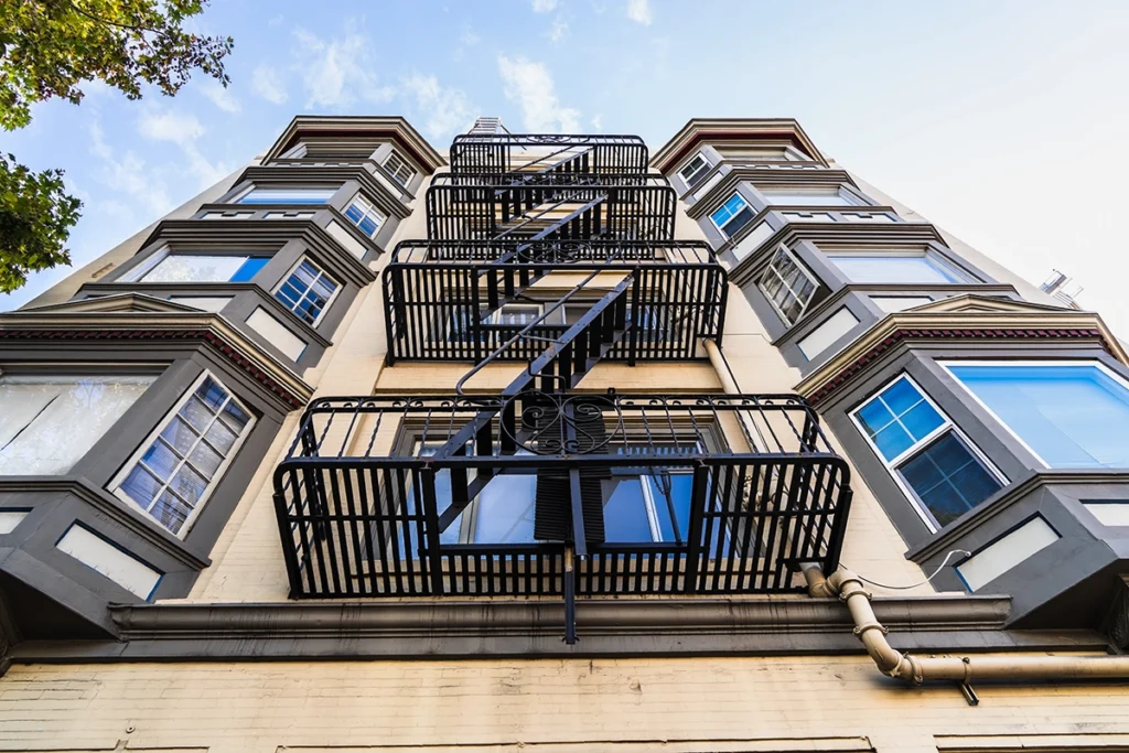 exterior of a multi-family apartment building with an emergency escape ladder zig zagging up the front between large bay windows