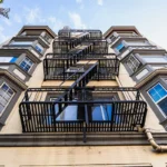 exterior of a multi-family apartment building with an emergency escape ladder zig zagging up the front between large bay windows