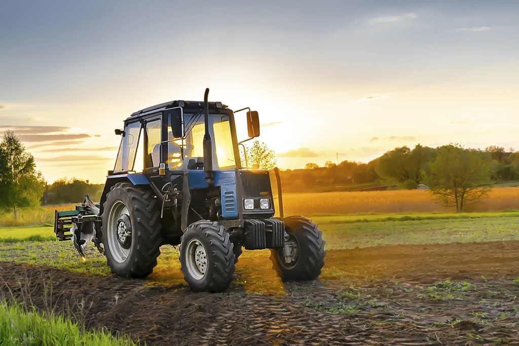 Farm tractor in front of a dramatic sunset on a field. Farm insurance to cover your equipment