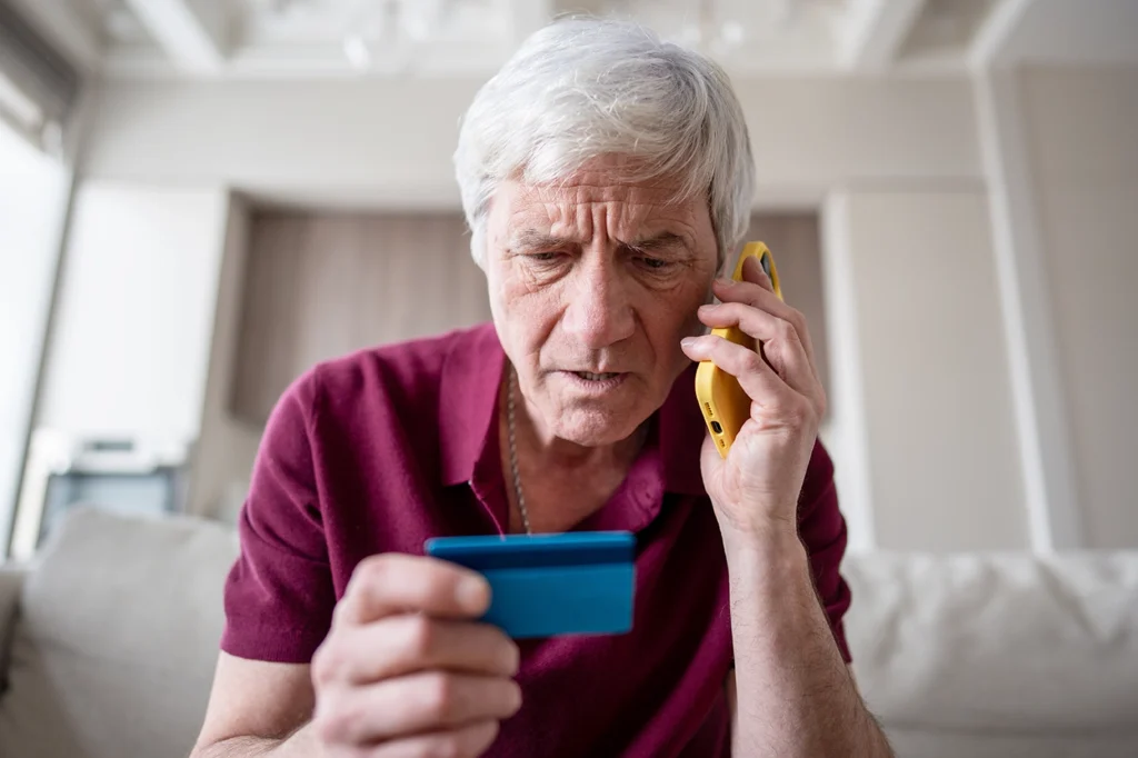 worried senior man on a phone looking at a credit card avoid scam calls